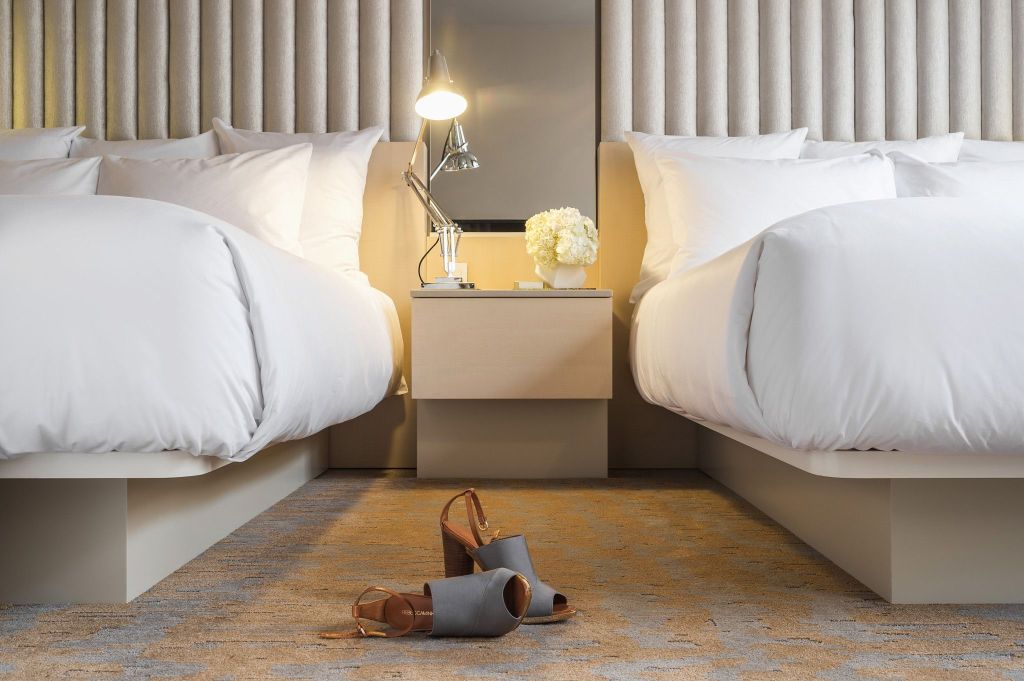 Two queen hotel beds with white bedding and a pair of stylish shoes on the floor