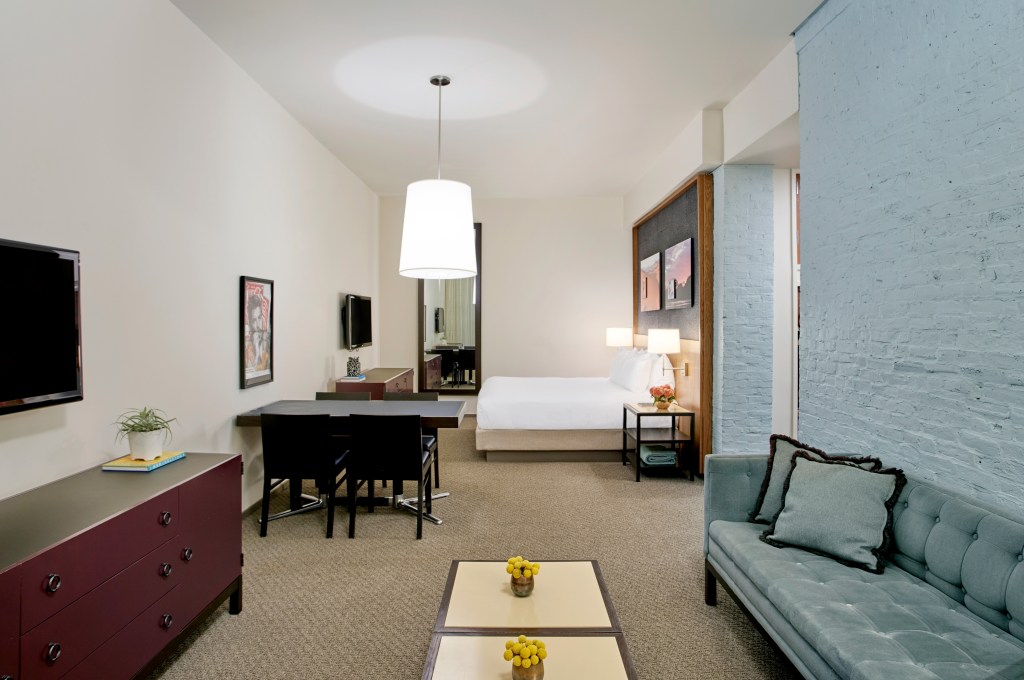 A hotel room with one king bed, a dining or working area and a living area with a small couch and coffee table