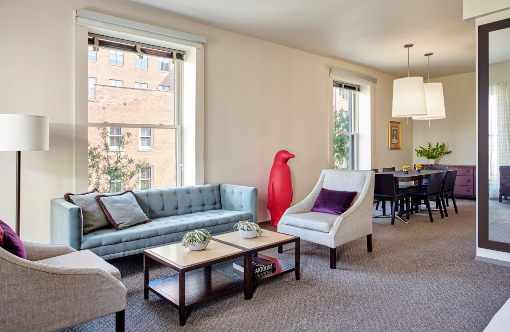 A hotel room living area with a couch, chairs, coffee table and 21c's iconic red penguin sculpture