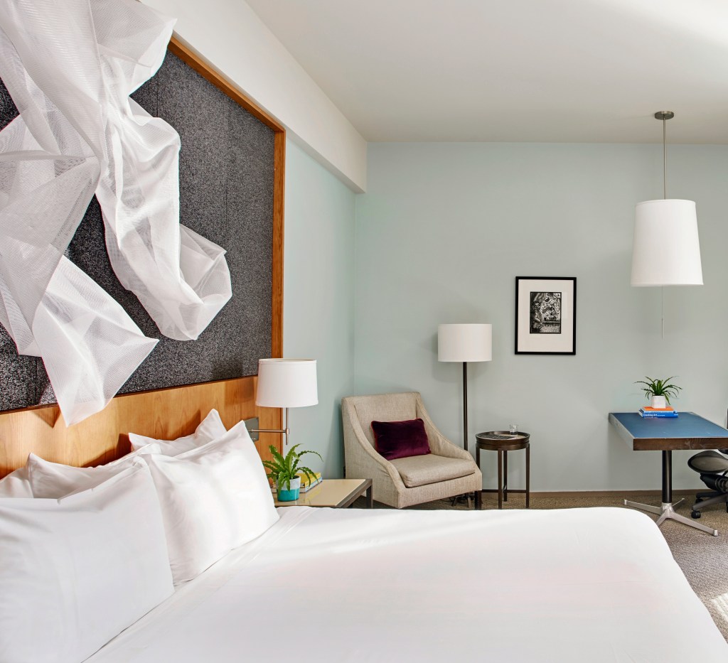 A hotel room with one king bed, a side chair, and a small office area