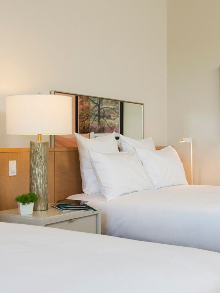 Two hotel beds with white bedding, a nightstand and lamp 