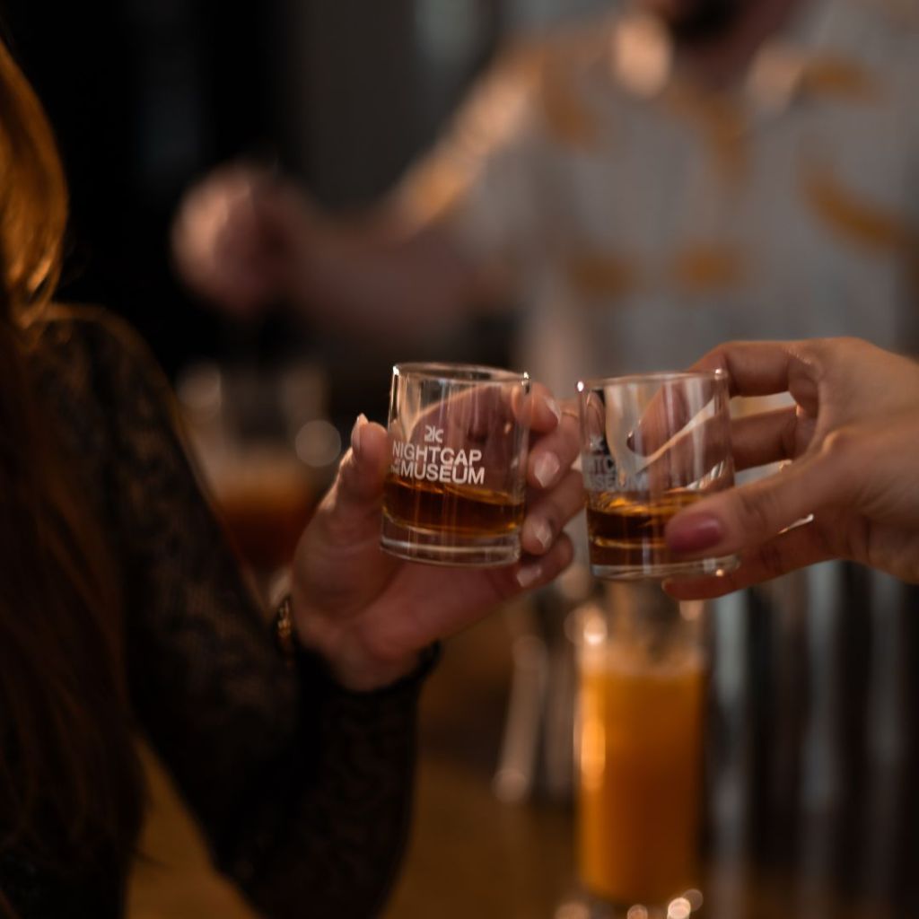 Closeup image of two glasses of bourbon held by hands toasting