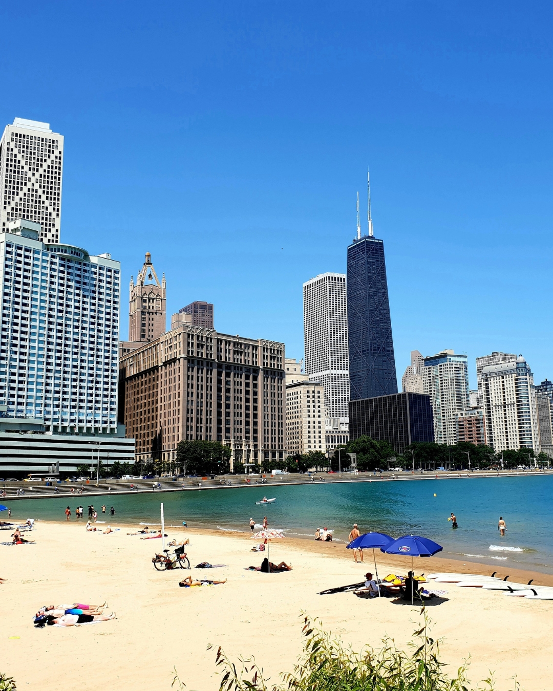 Small sandy beach with lake and city skyline with high rises in the background